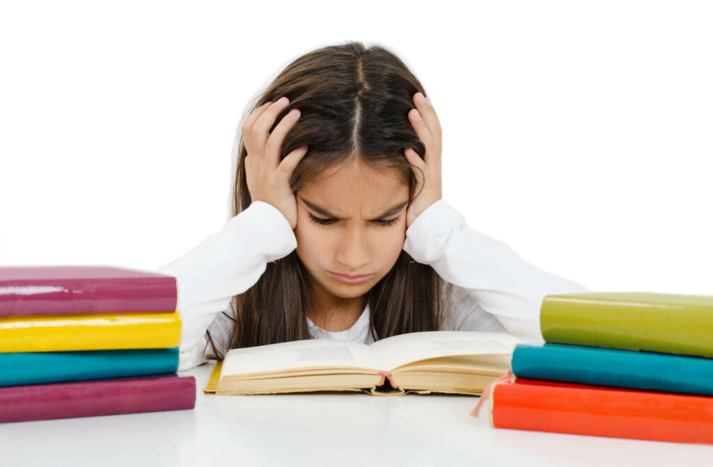 A young girl is frowning and her hands place on her head, having a hard time reading due to poor eyesight.