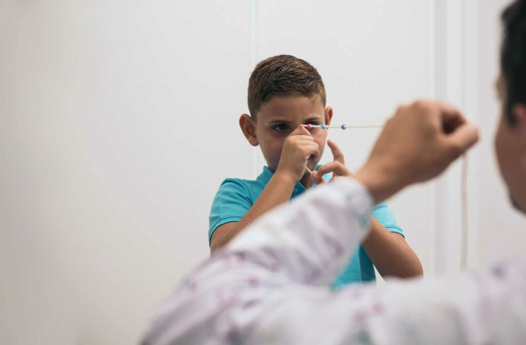 A boy is undergoing vision therapy with the use of a Brock cord. The boy is holding the string near his nose while his eyes are focusing on the beads and the optometrist is holding the other end.