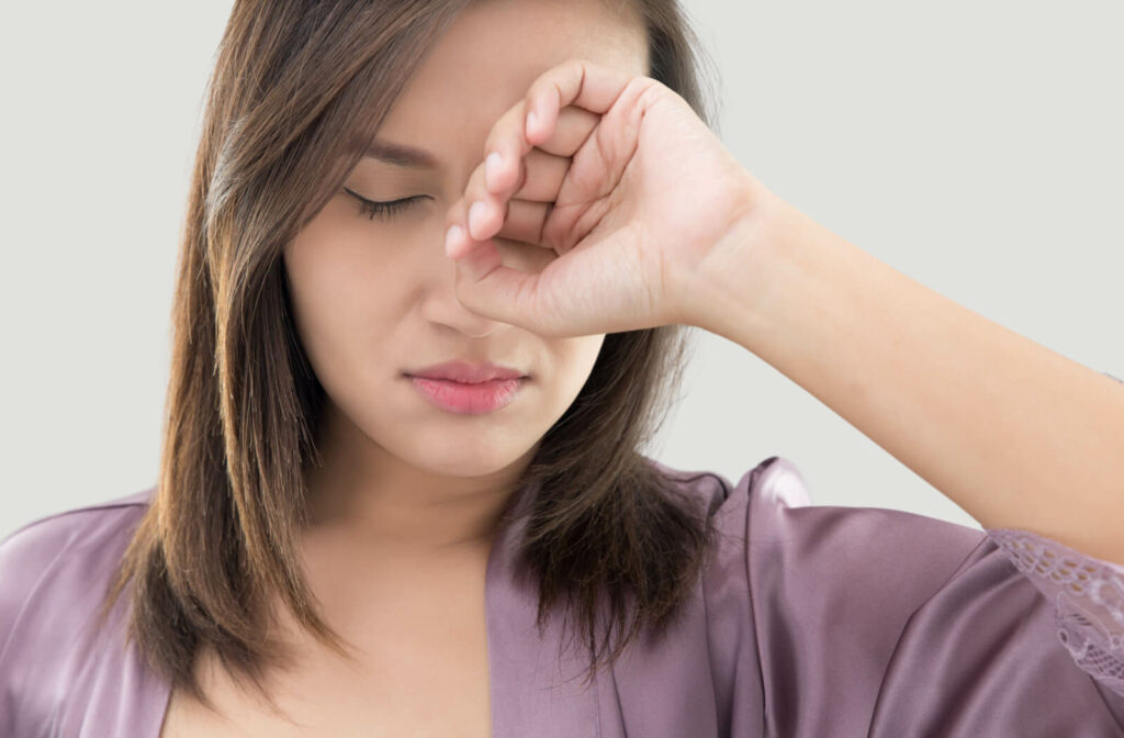 A woman in a purple robe rubbing her eye with her hand after waking with dry eyes.
