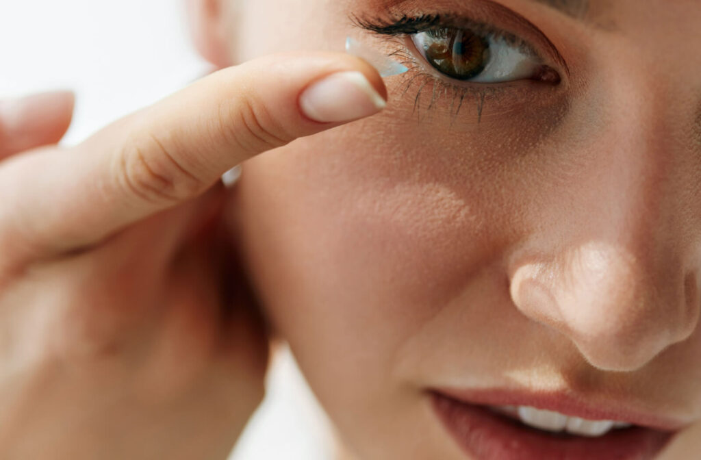 A woman putting on a contact lens on her right eye.
