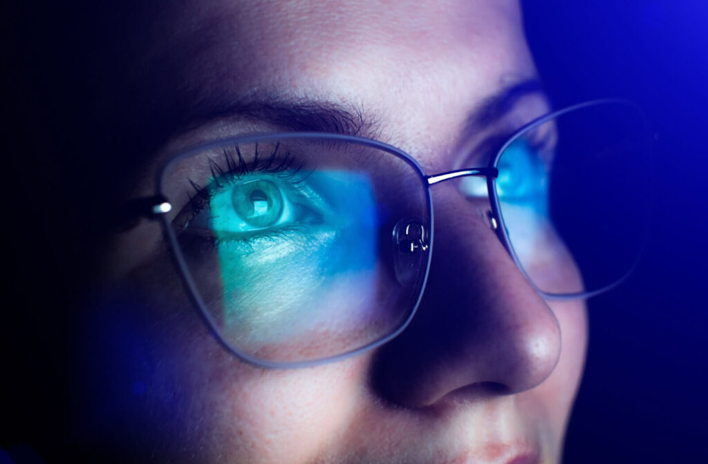 Close-up of a woman with blue light reflected on her glasses from a screen