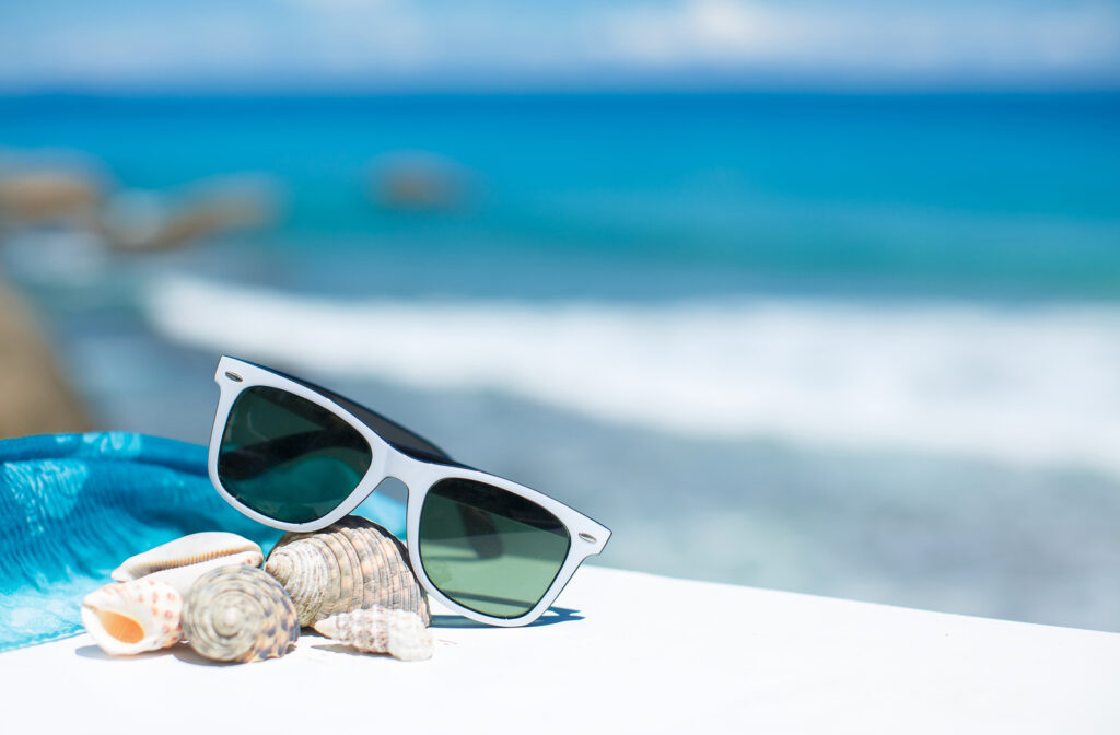 Grey sunglasses with dark lenses propped up on sea shells by the beach.
