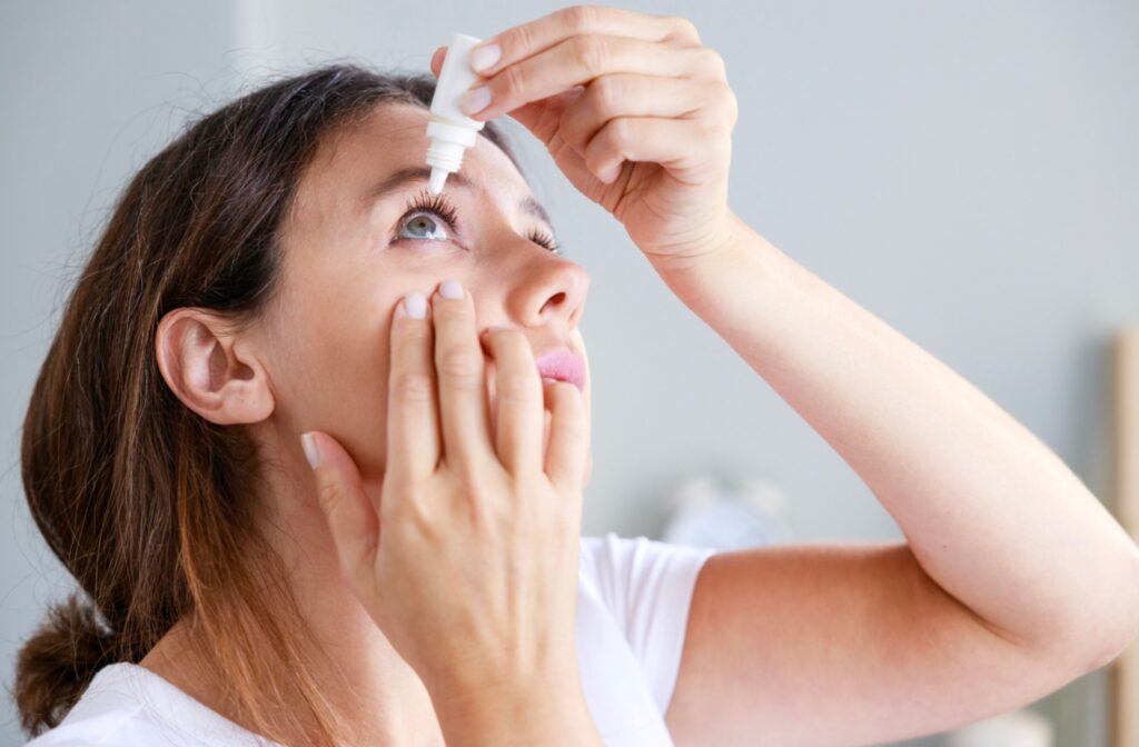 A young woman carefully applying eye drops to her right eye.